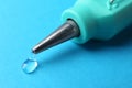 Melted glue dripping out of hot gun nozzle on light blue background, closeup Royalty Free Stock Photo