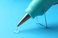 Melted glue dripping out of hot gun nozzle on light blue background, closeup Royalty Free Stock Photo