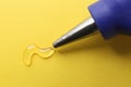 Melted glue dripping out of hot gun nozzle on yellow background Royalty Free Stock Photo