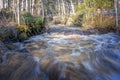 Melted snow water in forest creek runs through Scandinavian forest. Sunny spring day. Long exposure for smoothly flowing water. Royalty Free Stock Photo