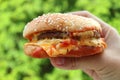 Melting cheese hamburger being held by hand against vibrant green foliage