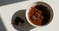 Melting chocolate squares in a white bowl under natural light, casting a soft shadow Royalty Free Stock Photo