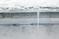 Melting icicle hangs from a snowy roof