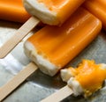 Melting orange creamsicles, one almost eaten, on a galvanized steel plate. Close up view.