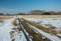 Melting snow on a dirt road through fields and wild meadows, coppice and clear sky Royalty Free Stock Photo