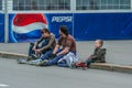 Members of a young family sitting on the side of road on background of Pepsi.