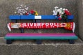 Seaside memorial bench decorated with flowers and a Liverpool Football Club scarf