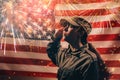 Memorial day. A female soldier in uniform salutes against the background of the American flag with fireworks. Side view. The Royalty Free Stock Photo