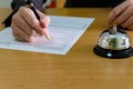 Men business person use pen to writing on a hotel reservation form at reception concierge desk. With a bell ring for guest to call