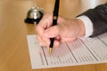 Men business person use pen to writing on a hotel reservation form at reception concierge desk. With a bell ring for guest to call