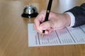 Men business person use pen to writing on a hotel reservation form at reception concierge desk. With a bell ring for guest to call