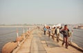 Men carry heavy bags of goods across the bridge over wide river Ganges Royalty Free Stock Photo