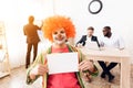 A man in a clown suit and a wig is sitting in the business office on April 1. Royalty Free Stock Photo