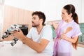 A man collects a robot in the kitchen. His girlfriend is behind him and very angry.