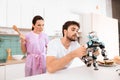 A man collects a robot in the kitchen. His girlfriend is behind him and very angry.