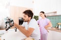 A man collects a robot in the kitchen. His girlfriend is behind him and very angry.