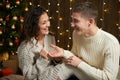 The man gives the girl an engagement ring, couple in christmas lights and decoration, dressed in white, fir tree on dark wooden ba Royalty Free Stock Photo