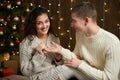 The man gives the girl an engagement ring, couple in christmas lights and decoration, dressed in white, fir tree on dark wooden ba Royalty Free Stock Photo