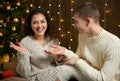 The man gives the girl an engagement ring, couple in christmas lights and decoration, dressed in white, fir tree on dark wooden ba