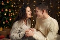 The man gives the girl an engagement ring, couple is in christmas lights and decoration, dressed in white, fir tree on dark wooden Royalty Free Stock Photo