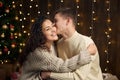 The man gives the girl an engagement ring, couple is in christmas lights and decoration, dressed in white, fir tree on dark wooden Royalty Free Stock Photo