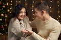 The man gives the girl an engagement ring, couple is in christmas lights and decoration, dressed in white, fir tree on dark wooden Royalty Free Stock Photo