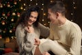 The man gives the girl an engagement ring, couple is in christmas lights and decoration, dressed in white, fir tree on dark wooden Royalty Free Stock Photo