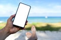 Men hand holding a white screen blank phone.He slept on the beach Royalty Free Stock Photo