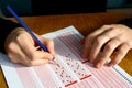 Hand with pencil filling out answers on exam test answer sheet Royalty Free Stock Photo