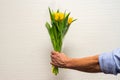 Men hand with yellow tulips bouquet on white brick wall background. Springtime. Woman and mother day concept Royalty Free Stock Photo