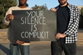 Men holding sign with phrase Your Silence Is Complicit outdoors, closeup. Racism concept