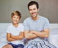 The men of the house. Portrait of a cheerful father and son seated on a bed with arms folded while looking at the camera Royalty Free Stock Photo