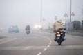 men on motorcycle covered with shawls riding on cold winter morning in dense fog with limited traffic in delhi, haryana