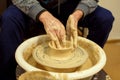 The men potters hands form by a clay pot on a potters wheel. The potter works in a workshop.