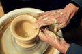 The men potters hands form by a clay pot on a potters wheel. The potter works in a workshop.