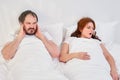 A man puts his hands over his ears because of the noise and snoring of a woman. Sleep problems in family relationships