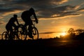 The men ride bikes at sunset with orange-blue sky background. Royalty Free Stock Photo