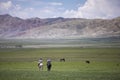 Men riding horses on the plains of Kyrgyzstan with mountains in the background