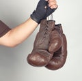 men's arm wrapped in a black elastic sports bandage holds pair old vintage leather boxing gloves Royalty Free Stock Photo