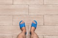 Men`s bare feet in blue home slippers stand on a light laminate floor tile background, view from above Royalty Free Stock Photo