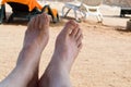 Men`s bare legs, feet against the backdrop of sun beds, deckchairs on the beach against the backdrop of a tropical resort Royalty Free Stock Photo