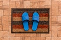 Men`s blue house slippers stand on a foot mat on a brown tiled floor texture background, top view Royalty Free Stock Photo