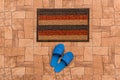 Men`s blue house slippers stand near foot mat on a brown tiled floor texture background, top view Royalty Free Stock Photo