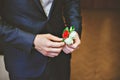 Men's blue suit, red tie, white shirt. The groom adjusts his boutonniere of roses.