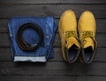 Men`s casual wear, yellow work boots from natural nubuck leather, blue jeans and brown belt on dark wooden background top view Royalty Free Stock Photo