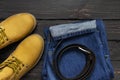 Men`s casual wear, yellow work boots from natural nubuck leather, blue jeans and brown belt on dark wooden background top view Royalty Free Stock Photo