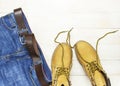 Men`s casual wear, yellow work boots from natural nubuck leather, blue jeans and brown belt on wooden white background top view Royalty Free Stock Photo