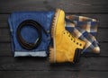 Men`s casual wear, yellow work boots from natural nubuck leather, blue jeans, checkered shirt and brown belt on dark wooden Royalty Free Stock Photo