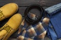 Men`s casual wear, yellow work boots from natural nubuck leather, blue jeans, checkered shirt and brown belt on dark wooden Royalty Free Stock Photo