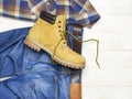 Men`s casual wear, yellow work boots from natural nubuck leather, blue jeans, checkered shirt and brown belt on wooden white Royalty Free Stock Photo